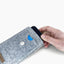 Ein Motorola Moto G15 wird von Hand aus einer stilvollen hellgrauen Handytasche mit Knopfverschluss gezogen.
