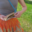 Person holding stylish Umhängetasche made of cork with adjustable strap outdoors.